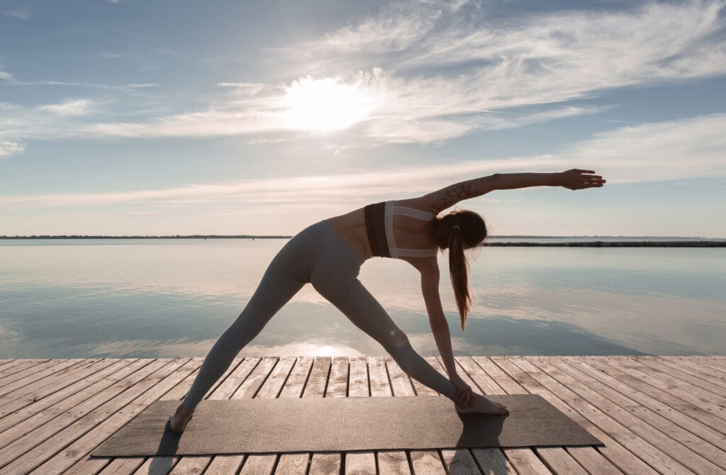 Woman practicing yoga at the edge of a serene lake, reflecting the harmony of yoga and meditation with nature.